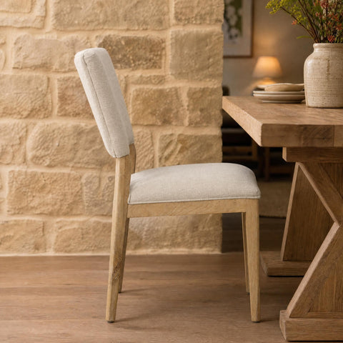 Side view of Lucile Dining Chair against textured stone wall in warm, inviting dining space with ambient lighting.