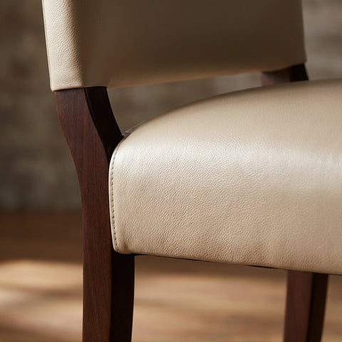 Close-up of the ClairLeather Chair's armrest, showcasing top grain leather and polished wood with detailed stitching and texture under soft natural light.