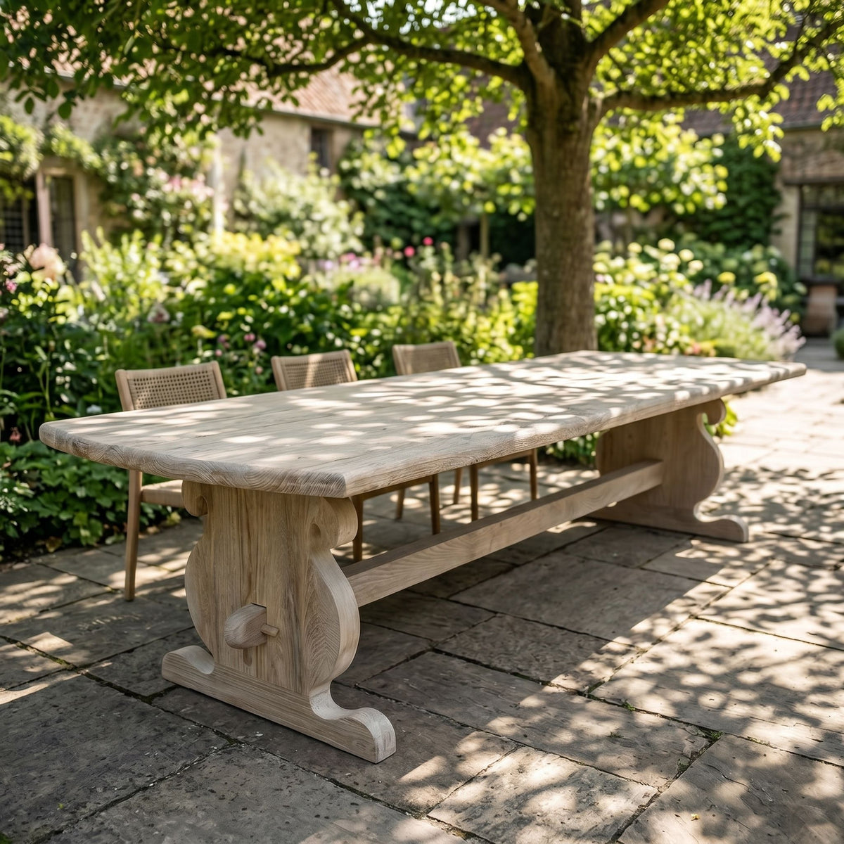Side view of weathered teak table in lush garden, highlighting its size and ornate details for outdoor dining.