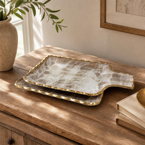 Large gold brushed tray with gold-bordered design resting on a textured wooden surface in a cozy home setting.