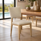 Elegant Lucile Dining Chair with oak frame and light sand upholstery in modern dining setting with natural lighting and wood floor.