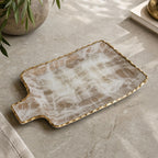 Large gold brushed tray with gold border seen from above on a matte stone countertop in an elegant environment.