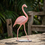 Petite flamingo sculpture sitting on textured natural stone in a rustic garden during daylight, showcasing its sleek lines and timeless craftsmanship.