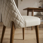 Detailed shot of Stitches dining chair's stitched diamond back, faux leather texture, and smooth oak legs with high-clarity lighting.