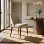 Full-body view of Stitches dining chair in a modern dining room, highlighting warm walnut oak legs, elegant silhouette, and natural daylight.